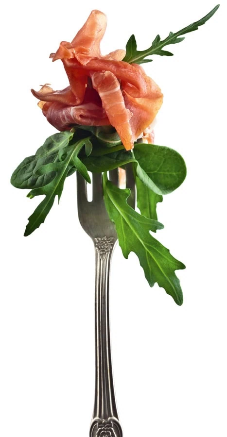 Silberne Gabel mit frischem Rucola und aufgerolltem Schinken auf der Spitze.